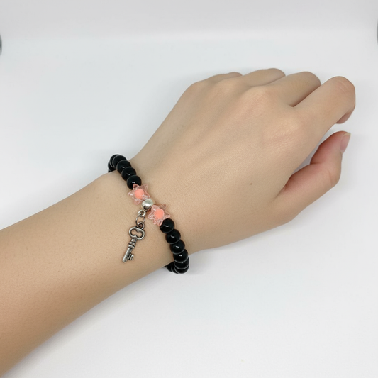 Hand wearing a black beaded bracelet with a key charm on a white background
