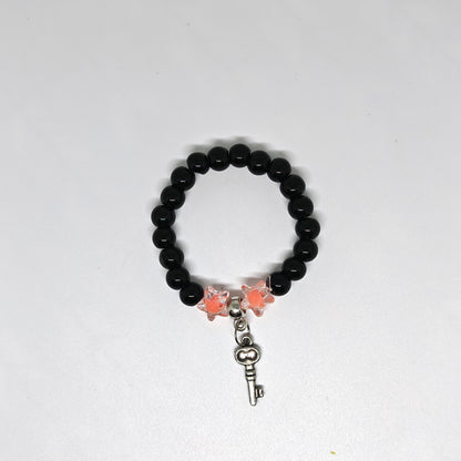 Black beaded bracelet with butterfly and key charm on a white background