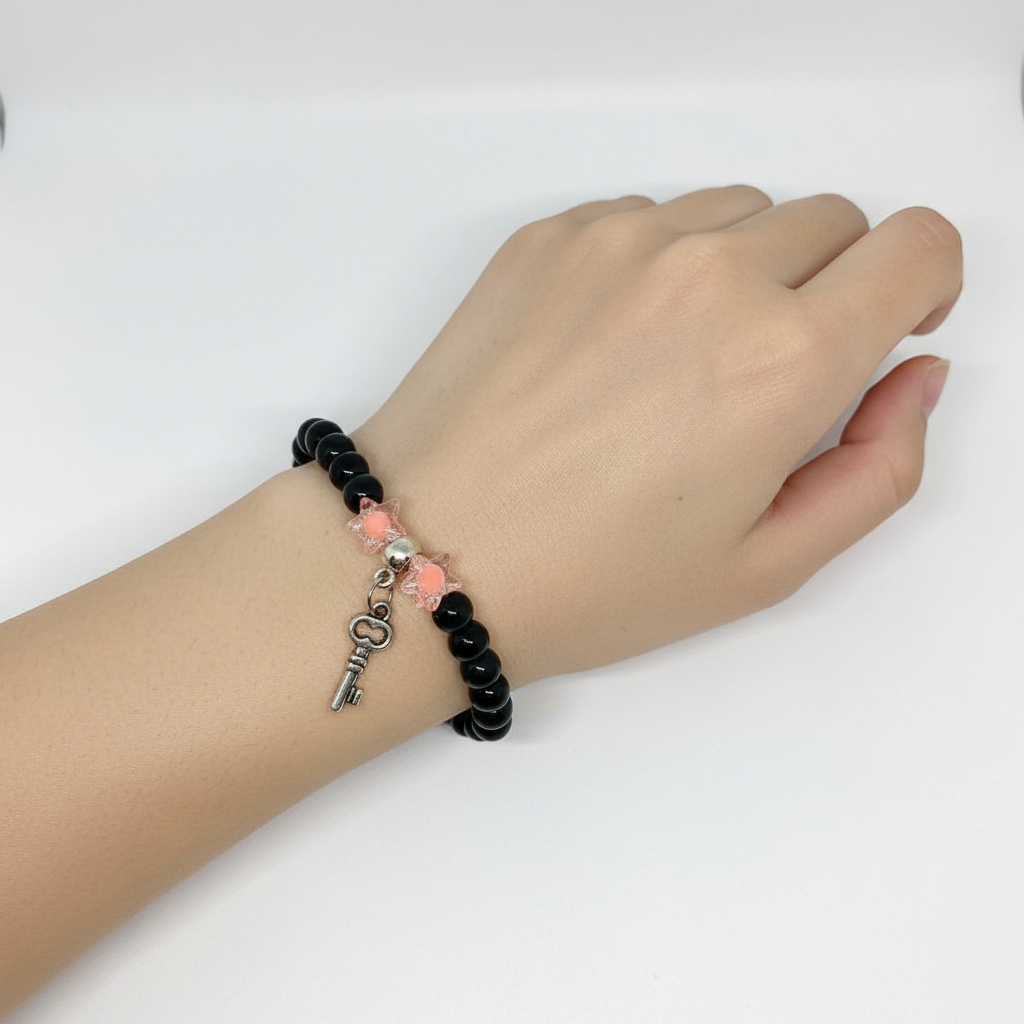 Hand wearing a black beaded bracelet with a key charm on a white background